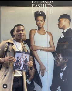 Talent featured in Black Fashion Fair Volume 0: SEEN holding the cover beside the storefront campaign.