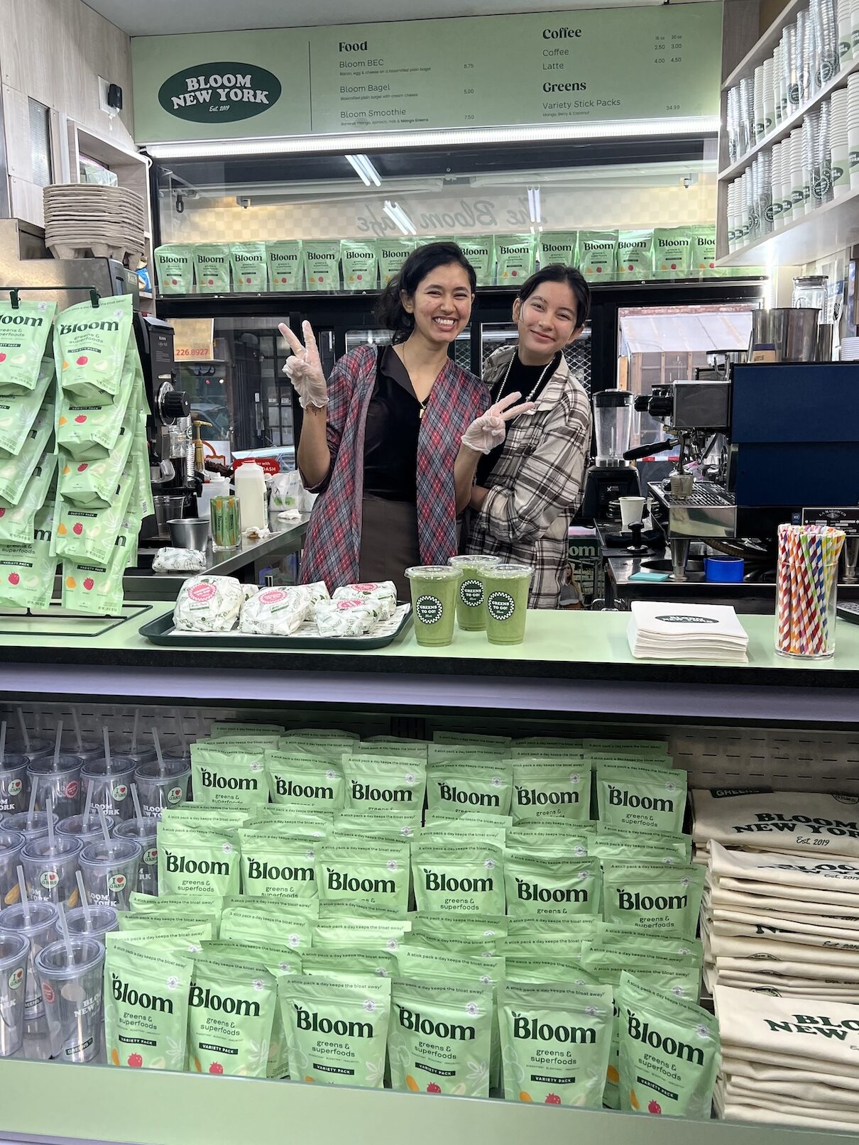 Bloom team members behind the counter with green smoothies, Greens powders, and branded merchandise.
