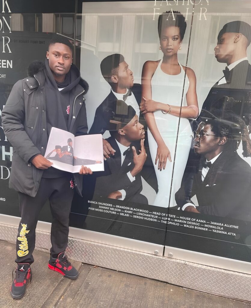 Talent featured in Black Fashion Fair Volume 0: SEEN holding the cover beside the storefront campaign.