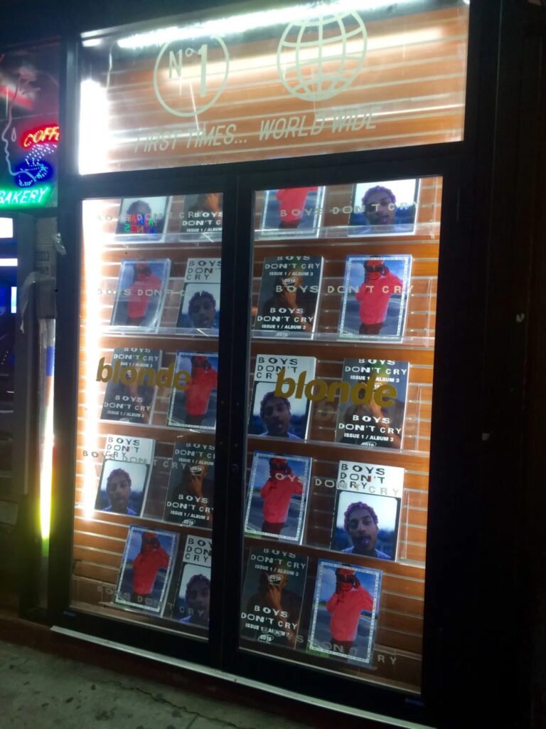 Illuminated storefront window filled with Frank Ocean’s Boys Don’t Cry magazine covers at night.